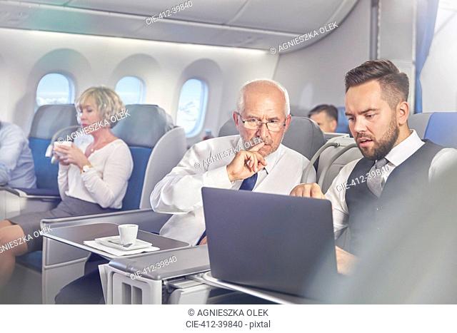 Businessmen working at laptop in first class on airplane