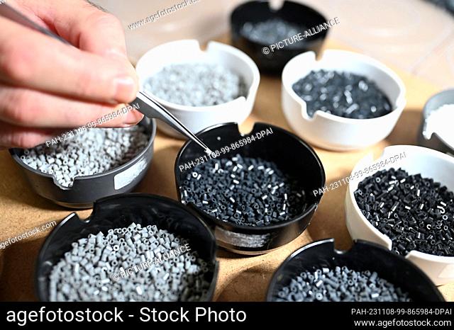 PRODUCTION - 07 November 2023, Baden-Württemberg, Pforzheim: Oliver Lemke removes an iron-on bead from bowls containing iron-on beads in various shades of gray...