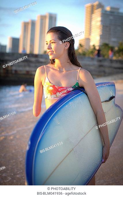 Mixed race amputee carrying surfboard on beach