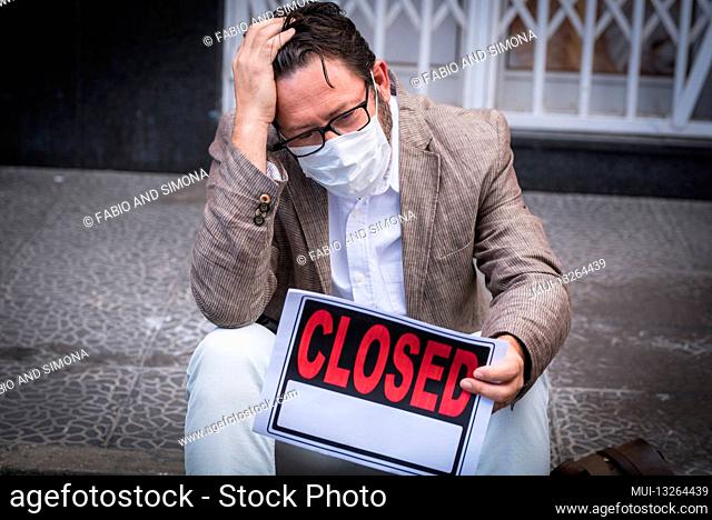 Portrait of desperate man wear medical mask for coronavirus economy crisis with closed business and for sale panel - concept of unemployed people after covid-19...