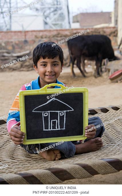 Portrait of a boy showing chalk drawing of house on a slate, Hasanpur, Haryana, India