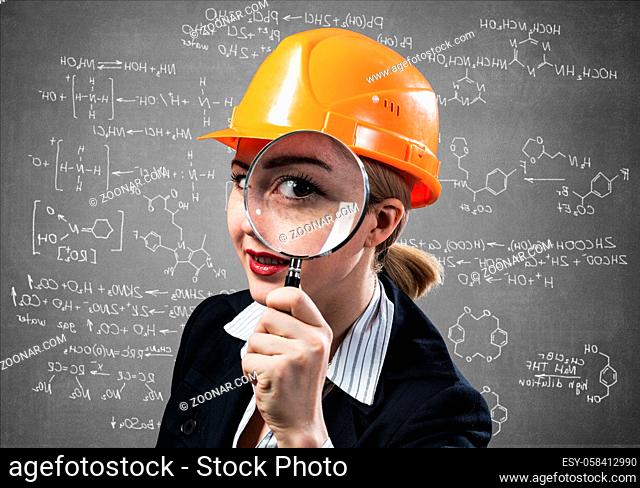 Professional appraiser looking through magnifying glass. Woman civil engineer in safety helmet checking with magnifier on wall background