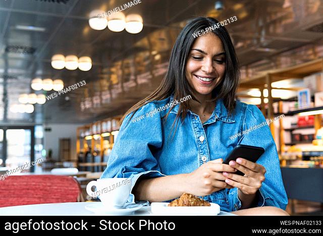 Smiling businesswoman using mobile phone while sitting in coffee shop