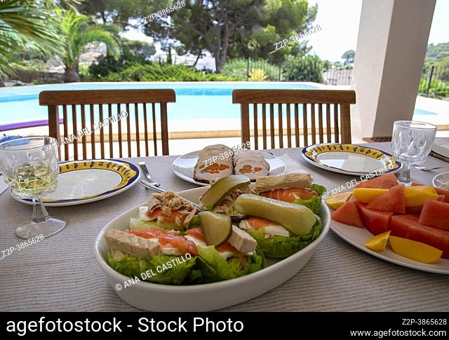 salad with salmon and tuna fruit and meat loaf on a table on the porch of a villa with a pool