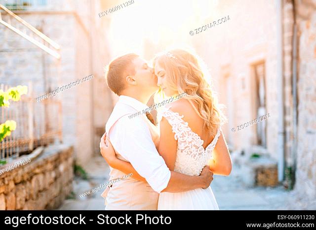 The bride and groom stand embracing on the streets of Perast, the groom kisses the bride on the forehead . High quality photo