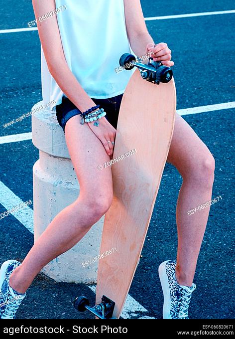 Girl-skater sitting in skate park with her longboard between her bare legs
