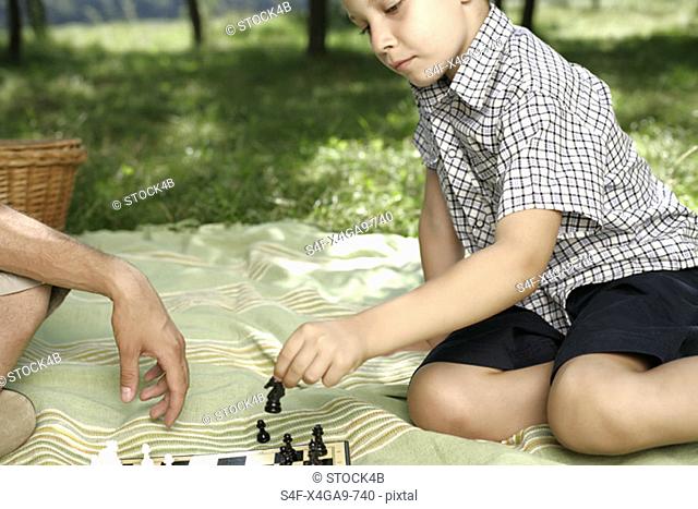 Father and son playing chess on a blanket