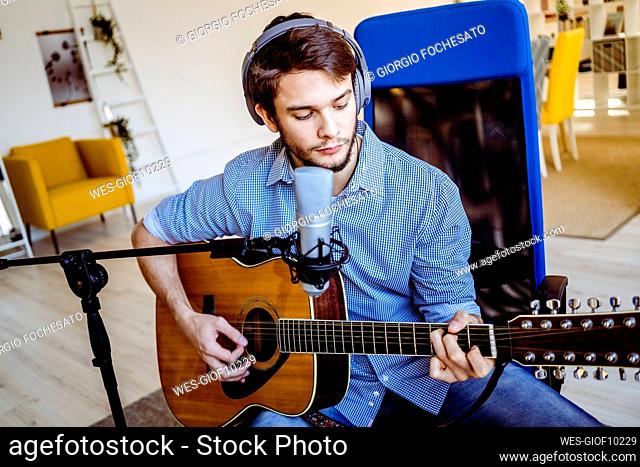 Professional with headphones and microphone playing guitar while sitting at recording studio
