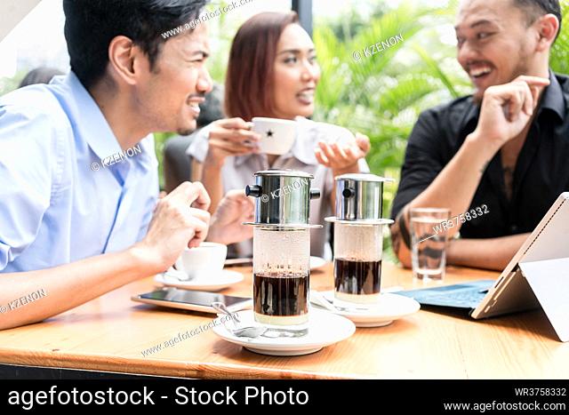 Delicious Vietnamese coffee served on the table of three young cheerful Asian friends outdoors in a modern cafeteria