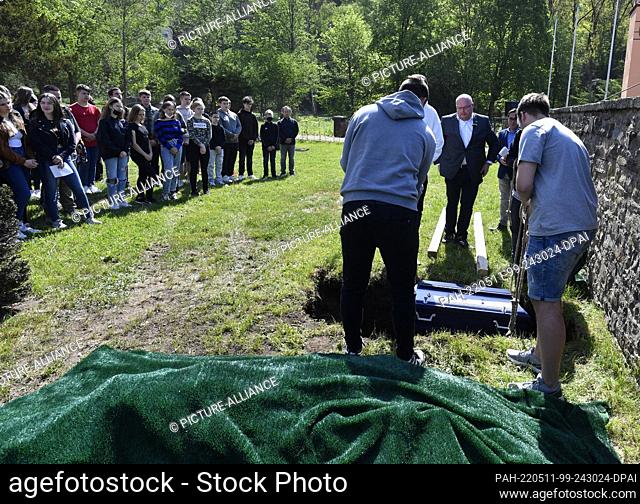 11 May 2022, North Rhine-Westphalia, Schleiden: Pupils of the Johannes-Sturmius-Gymnasium let the coffin into the grave with the bones of a school skeleton at...