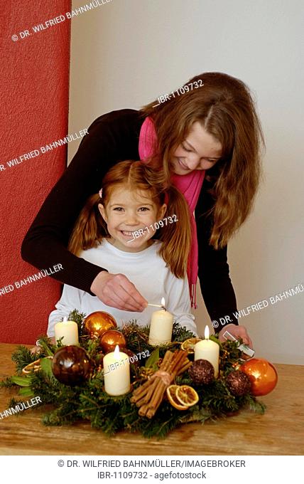 Young woman and her daughter are lighting candles on an advent wreath