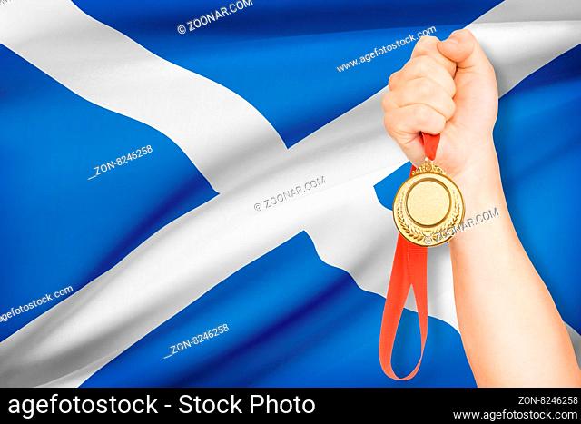 Sportsman holding gold medal with flag on background - Scotland