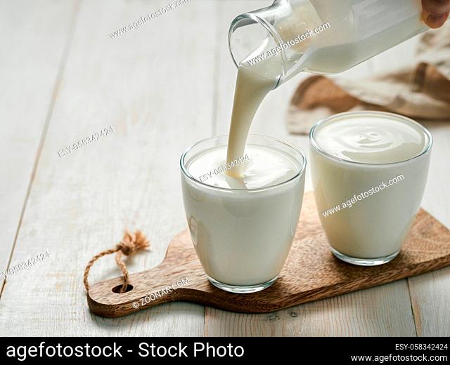 Pouring homemade kefir, buttermilk or yogurt with probiotics. Yogurt flowing from glass bottle on white wooden background