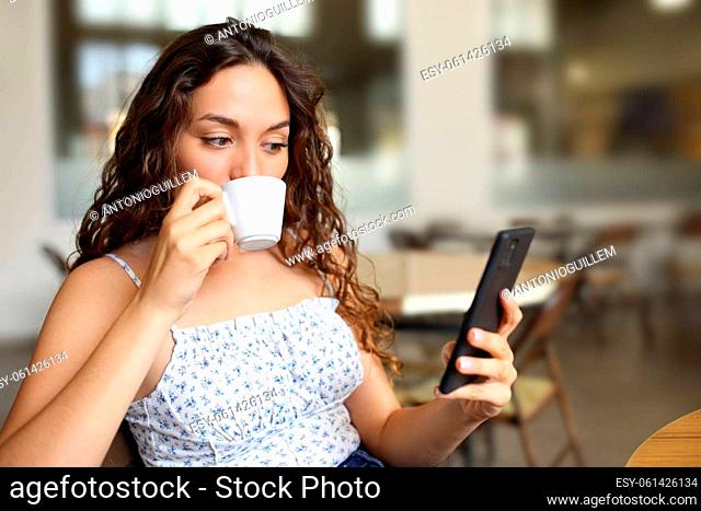 Woman drinking coffee and checking smart phone sitting in a bar