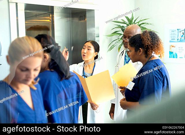 Diverse group of male and female doctors holding files discussing in busy hospital corridor