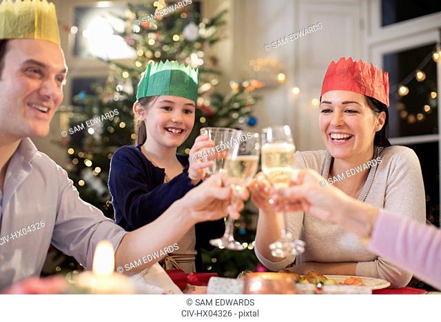 Happy family in paper crows toasting water and champagne glasses at Christmas dinner