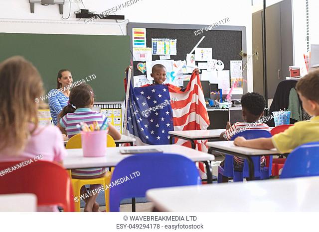 Front view of an African schoolboy holding an american flag in classroom at school while his classmates looking at him