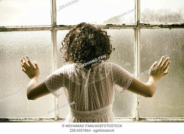 Rear view of a woman standing by the window hands touching the glass
