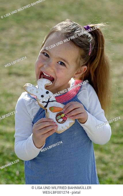 Portrait of smiling little girl biting off pastry formed like an Eastern Bunny