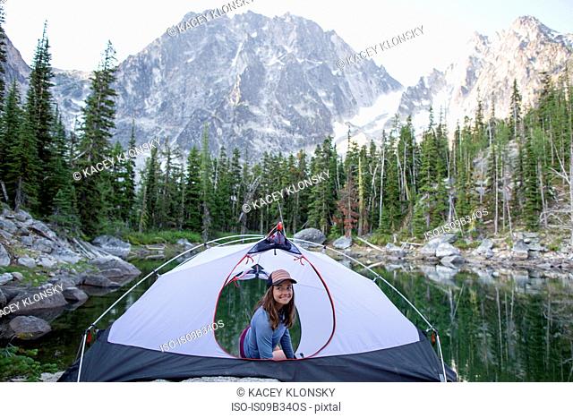 Young woman sitting in tent beside lake, The Enchantments, Alpine Lakes Wilderness, Washington, USA
