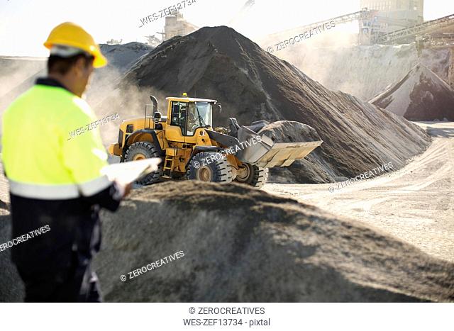 Worker standing at quarry, using clipboard