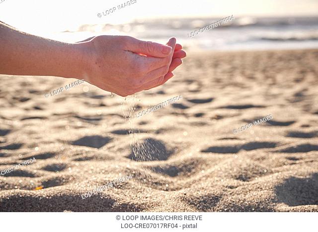 A young woman sifting sand through her hands on the beach