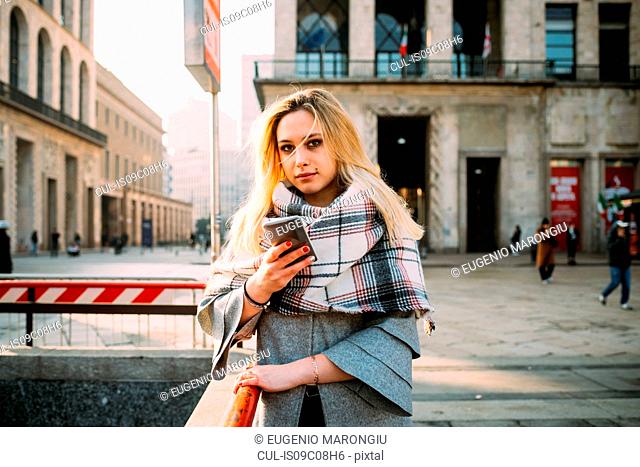 Young woman with smartphone by underground station, portrait, Milan, Italy