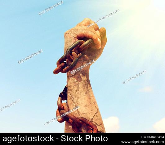 the female hand is wrapped in an iron rusty chain and raised up in the sun's rays against the sky