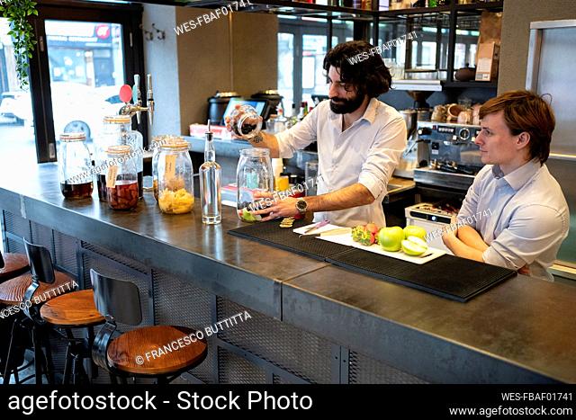Trainee looking at male bartender putting fruits in jar at bar counter