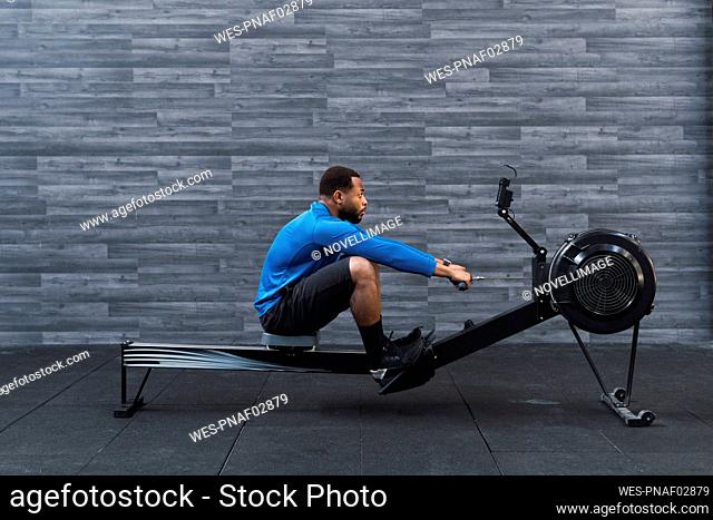 Concentrated athlete exercising on rowing machine in front of wall in gym