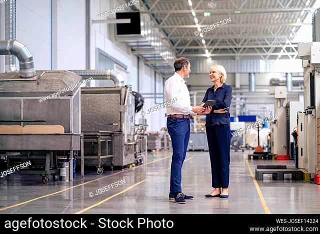 Mature businessman holding tablet PC discussing with colleague in factory