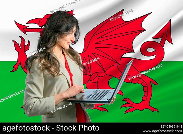 Freelance in Wales. Beautiful young woman freelancer uses laptop computer against the background of the flag of Wales