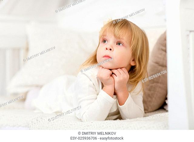 Serious pretty little girl lies on a sofa in the room and looks upwards