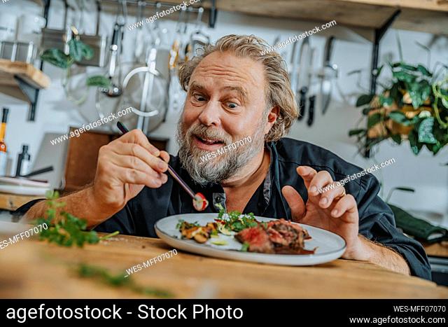 Mature chef garnishing tomahawk steak with vegetables while standing in kitchen