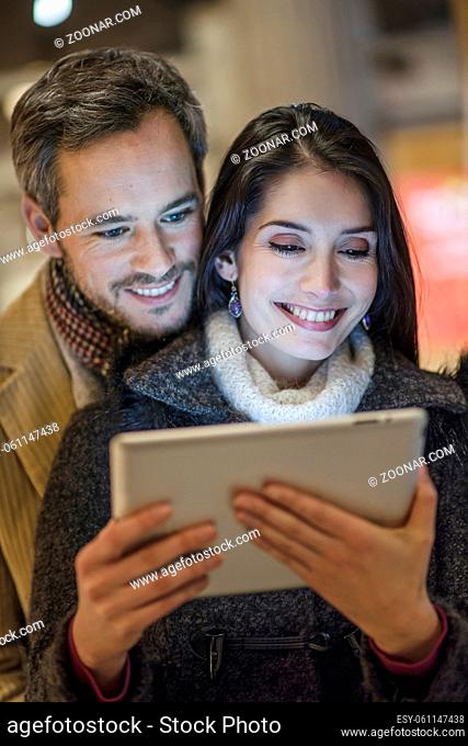handsome couple using a digital tablet outside with city lights at the background