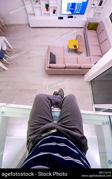 man sitting upstairs on glass floor while looking at the inside of a stylish duplex apartment