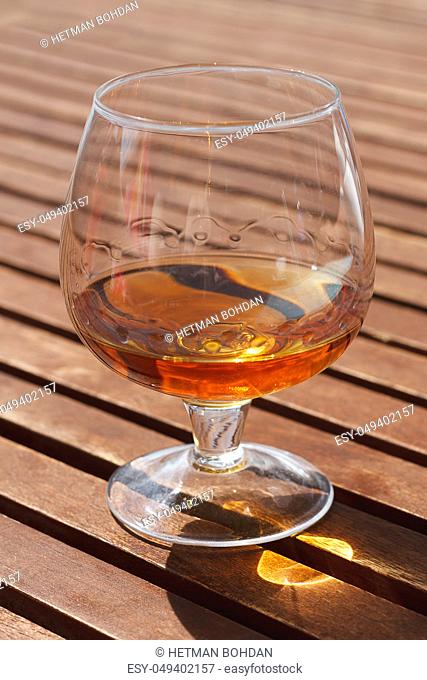 Glass of cognac standing on a wooden table in sunlight