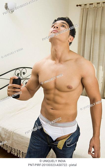 Man applying deodorant in a bedroom