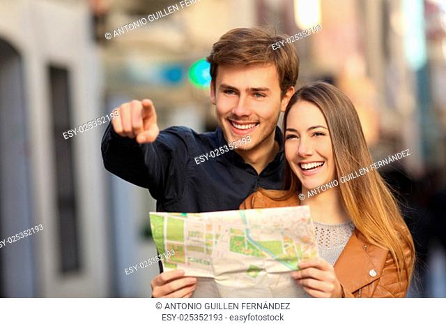 Happy couple of tourists on vacations searching a street in a map and pointing away