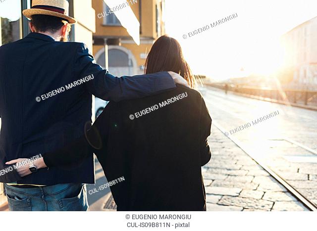 Rear view of couple strolling along sunlit sidewalk