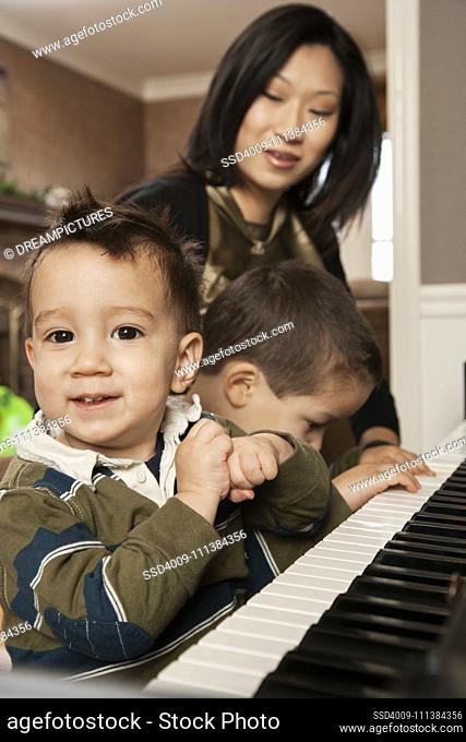 Asian mother teaching sons to play piano