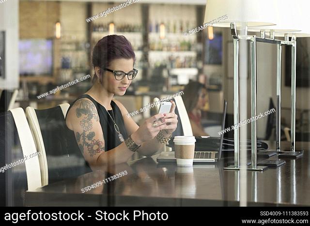 Caucasian woman using cell phone and laptop in coffee shop