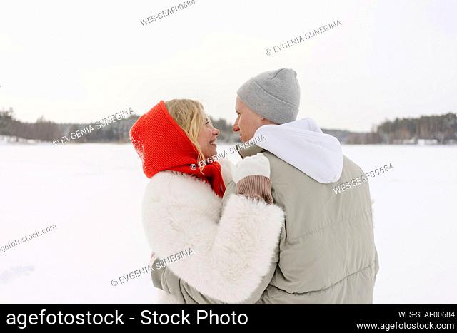Smiling woman looking at boyfriend wearing knit hat in winter