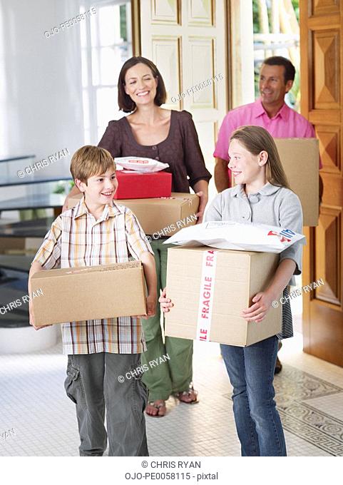 Couple with young boy and girl carrying boxes into home