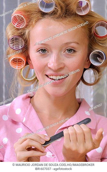 Redheaded woman wearing pajamas with curlers in her hair filing her nails