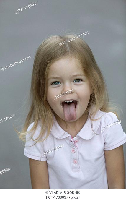 Portrait of cheerful girl sticking out tongue against gray background