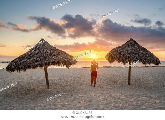 Bavaro Beach, Bavaro, Higuey, Punta Cana, Dominican Republic. Woman by thatch umbrellas on the beach at sunrise (MR)