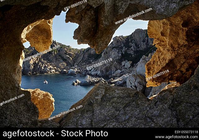 View of a natural bay on the southern coast of Sardinia filtered by the rocky walls of a cave on the opposite hill. Location Capo Ferrato