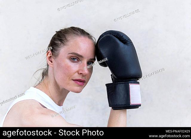 Serious female boxer with boxing glove in front of wall