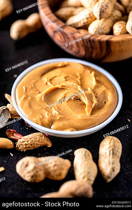 Peanut butter in bowl and peanuts on black table
